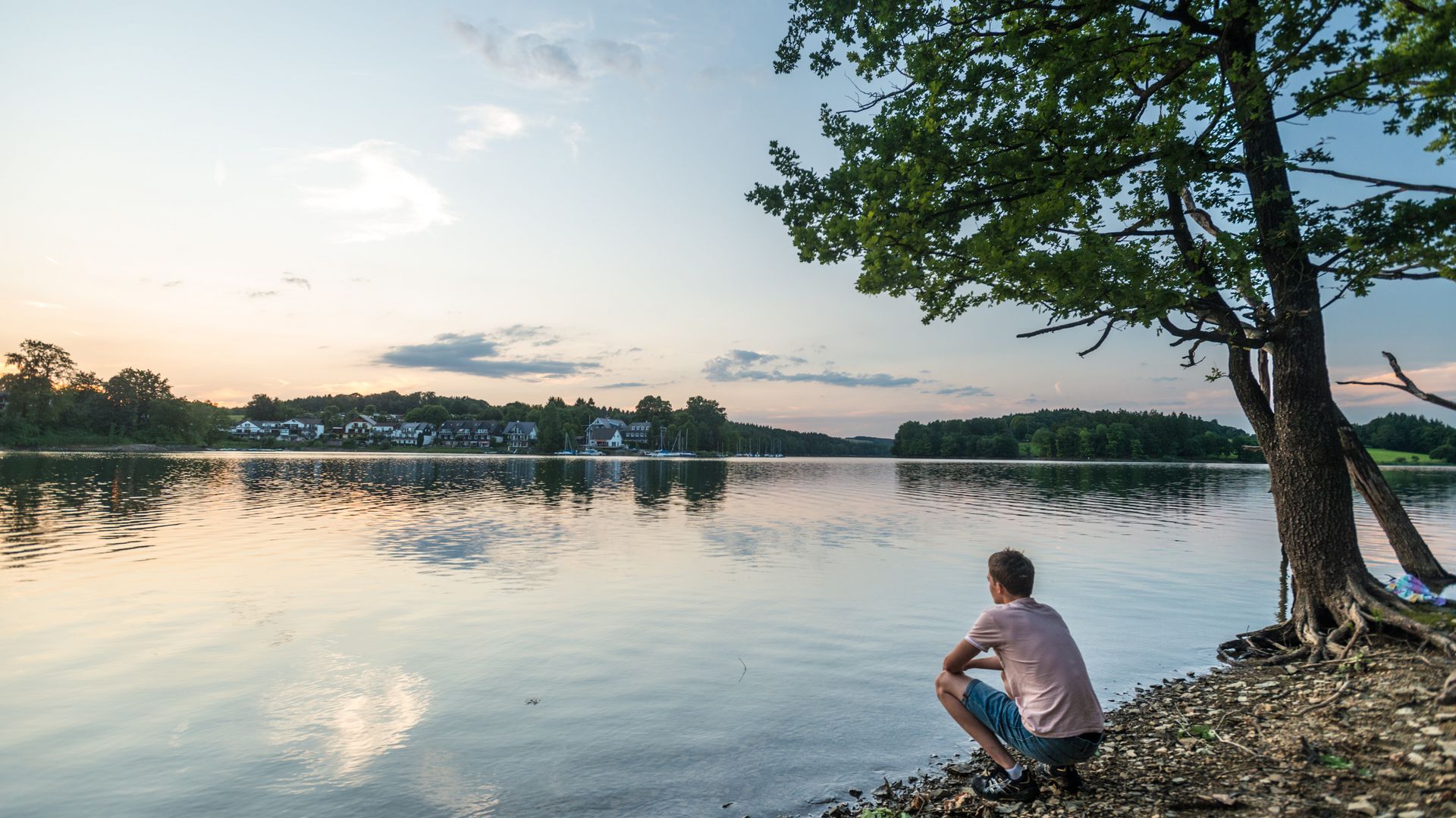 Junger Mann hockt in der Dämmerung am See