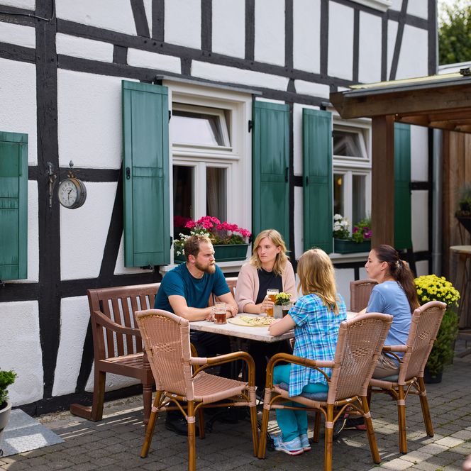 Vier Personen sitzen an einem Tisch vor einem Fachwerkhaus und genießen gemeinsam eine Mahlzeit.