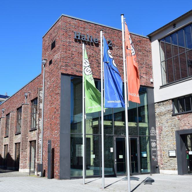 Halle 32 Gummersbach, modernes Kulturzentrum in einem sanierten Ziegelbau mit bunten Flaggen davor.