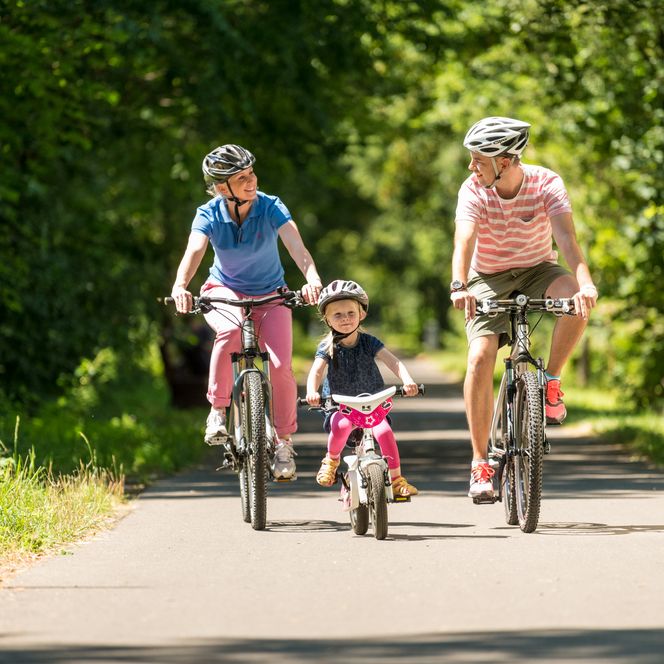 <p>Familie mit einem Kind auf Fahrrädern genießt eine Fahrt auf einem sonnigen Waldweg.</p>