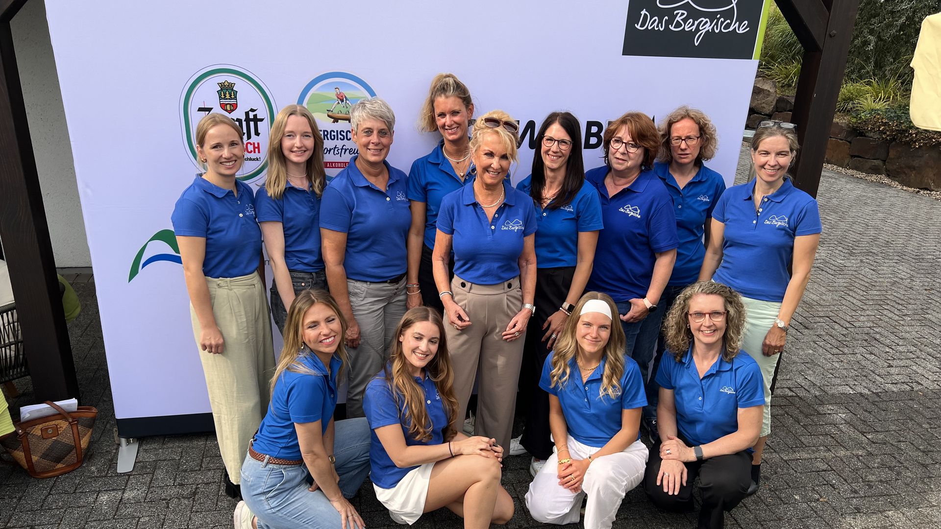 Das Team von "Das Bergische" steht vor einer Infowand. Alle tragen blaue Shirts.