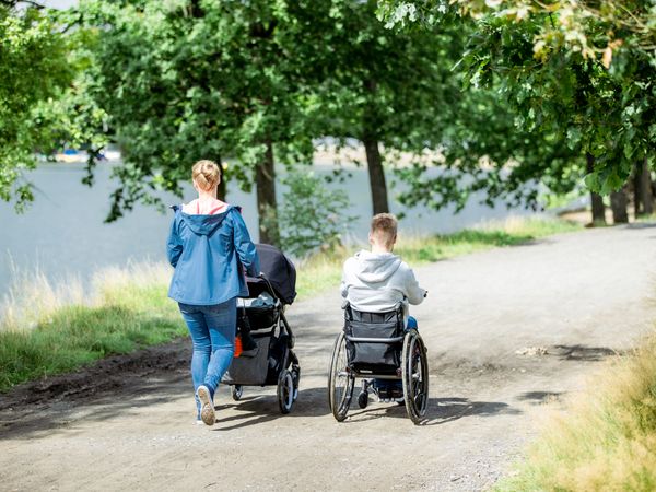 Eine Frau schiebt einen Kinderwagen, neben ihr fährt ein Mann im Rollstuhl am Ufer einer Talsperre.