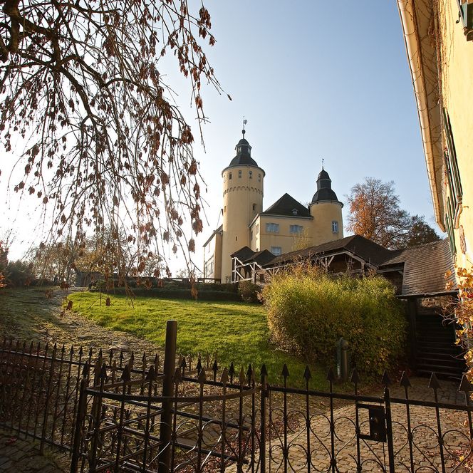 Schloss Homburg in Nümbrecht mit herbstlichem Garten und leuchtendem Turm bei Sonnenuntergang.