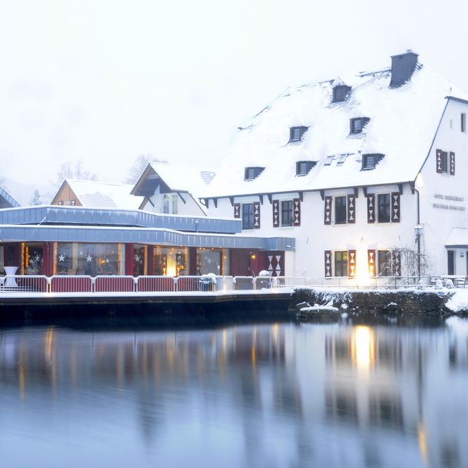 Hotel Gronau am winterlichen Seeufer in Bergisch Gladbach, mit verschneiten Dächern und warmem Licht.