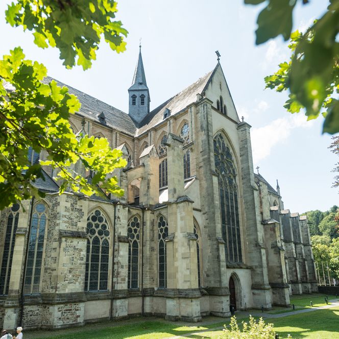 <p>Gotische Kirche im Grünen bei Sonnenschein, von Bäumen umrahmt, in Odenthal.</p>