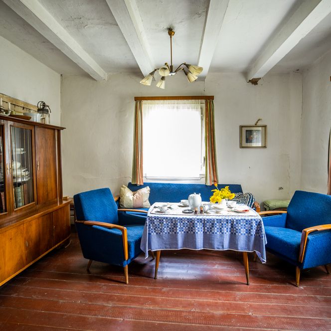 Wohnzimmer mit blauer Polstergarnitur, Holzboden, Schrank und gedecktem Tisch in rustikalem Stil.