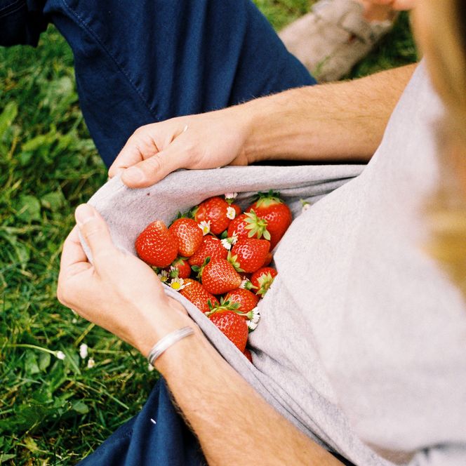 Frisch gepflückte Erdbeeren liegen in einem hochgezogenen T-Shirt auf einer Wiese
