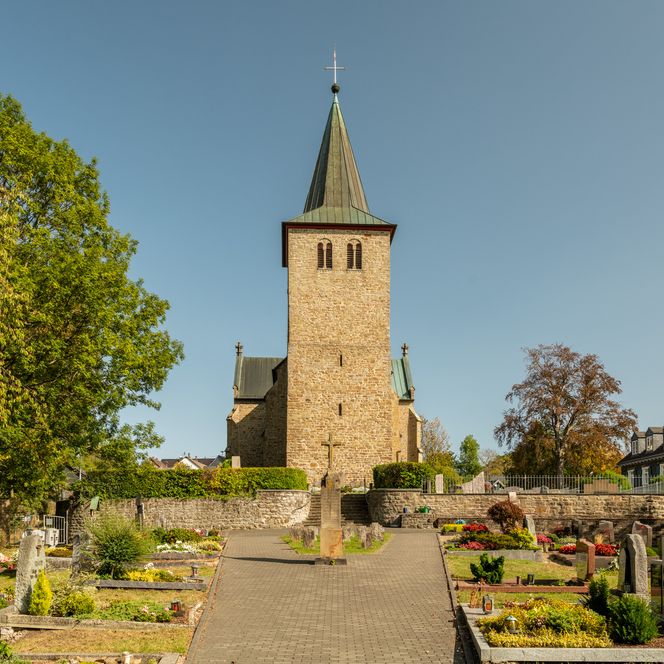 Die romanische Kirche von Neunkirchen-Seelscheid mit Friedhof im Vordergrund bei sonnigem Wetter.